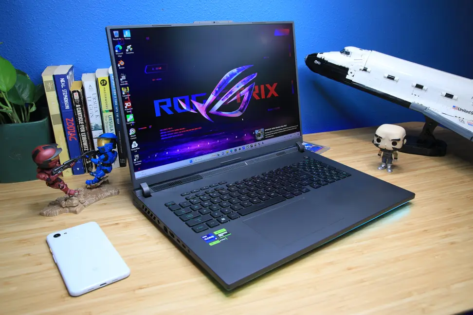 An open and powered on laptop sitting on top of a desk flanked by various objects