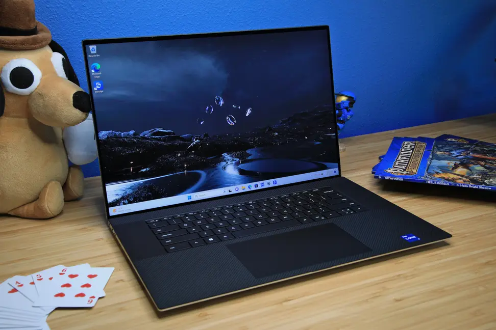 A powered-on and open laptop sitting on a light brown, wooden desk, flanked by knickknacks.