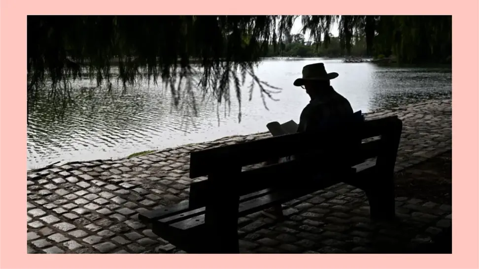 A person in a hat reads a book at the Regatas Lake in Buenos Aires.