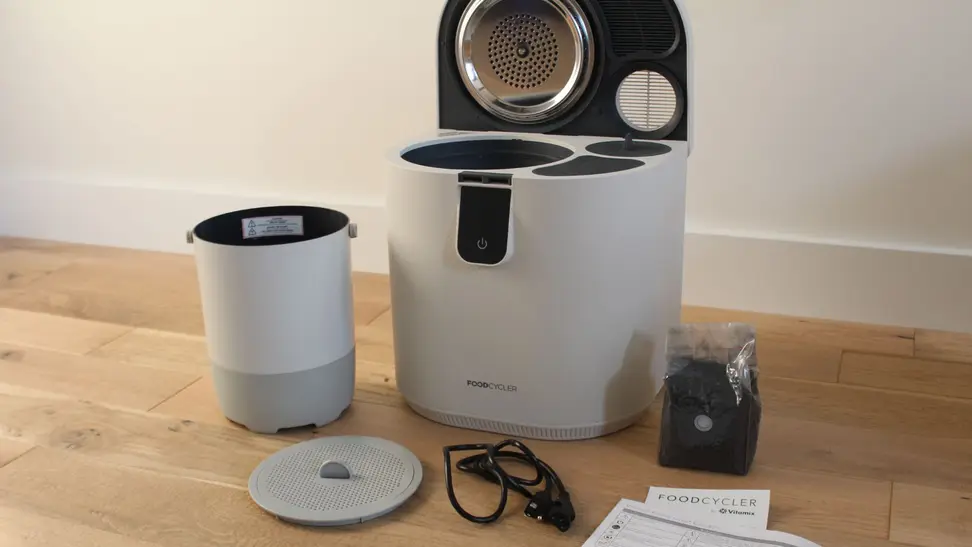 The Vitamix Eco 5 FoodCycler next to a plastic measuring cup with compost in it.