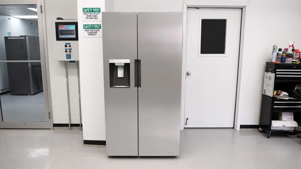 Stainless steel Midea MRS26D5AST Side-by-Side Refrigerator in front of white wall and white door.