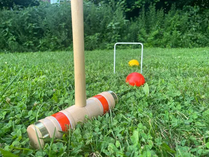 A croquet mallet, ball, and wicket on grass