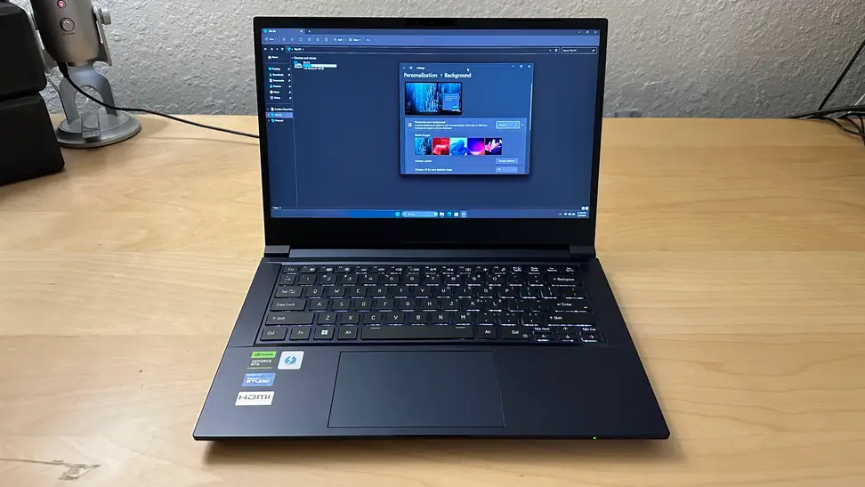 Origin EON14-S gaming laptop sitting on top of wooden surface with screen display turned on.