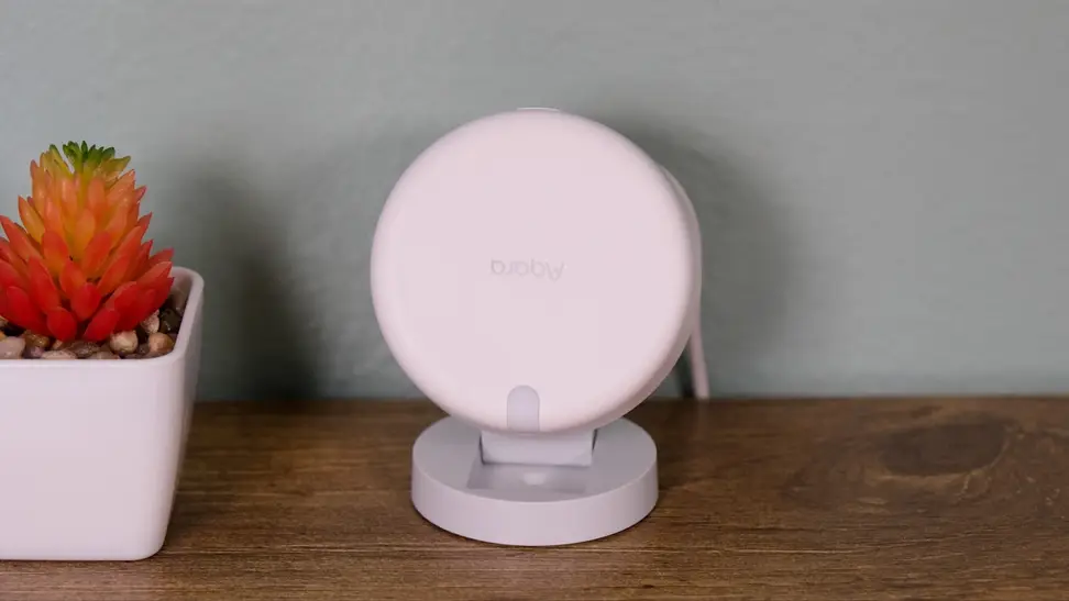 The Aqara FP2 presence sensor sits on its stand on a wood stand next to a potted red succulent plant.