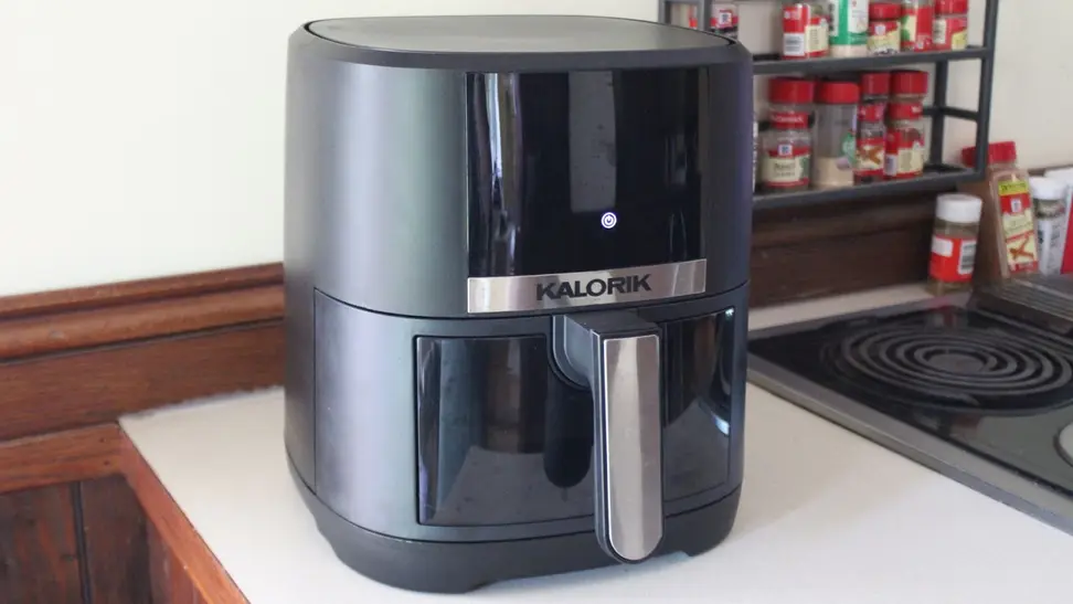 Black and stainless steel Kalorik 5-Quart Digital Air Fryer sitting on top of kitchen counter next to cooktop and filled spice rack.