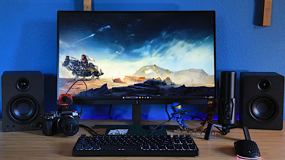 The Monoprice Dark Matter 27-inch 165Hz IPS gaming monitor next to two speakers, on a desk, with a blue background.