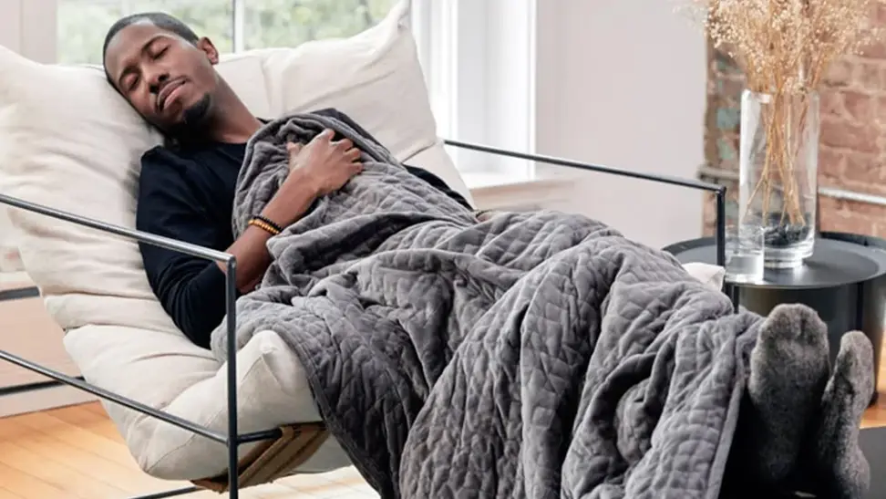 A man resting on a chair with a Gravity weighted blanket.