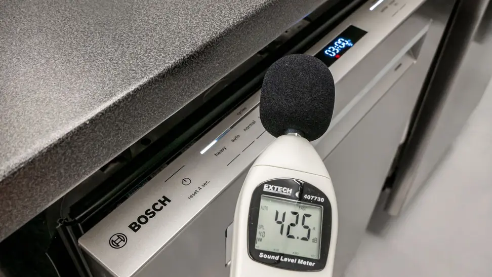 A decibel meter held in front of a dishwasher with a 42.5 reading on the screen.