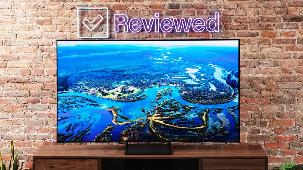 The Samsung S90C QD-OLED TV displaying colorful 4K content in front of a brick wall