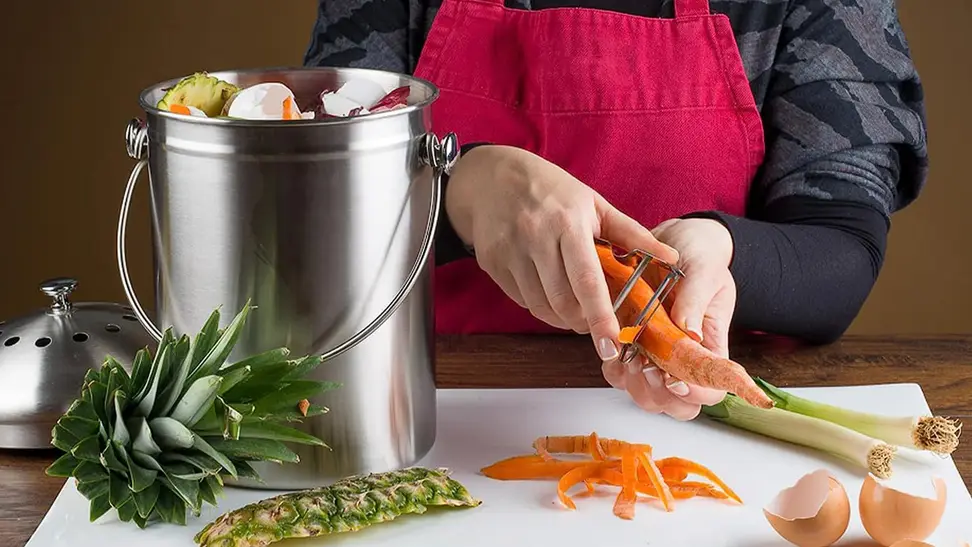 An Epica compost bin next to someone cutting up food in a kitchen.