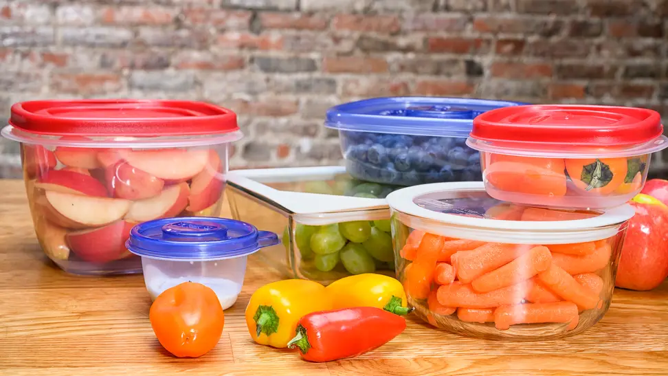 Several food strage containers filled with fresh produce on a wooden surface
