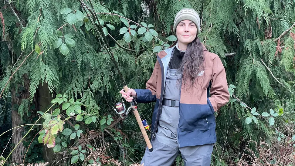 A woman wearing Simms fishing clothes and holding a fishing rod.