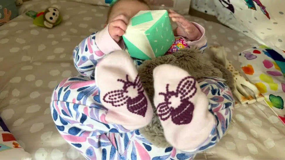 A baby wearing a Burt's Bees Baby onesie and holding a baby toy.