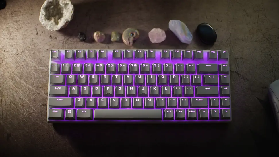 The Alienware Pro Keyboard mini with purple LED lights glowing inside the keyboard, surrounded by crystals and shells.