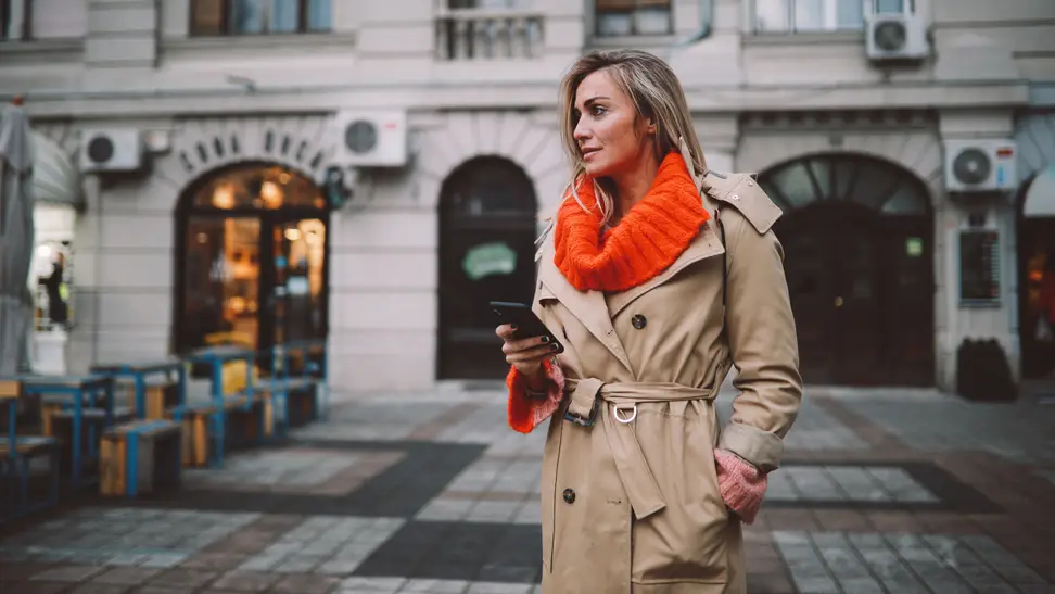 A woman wearing a trench coat with an orange sweater underneath.