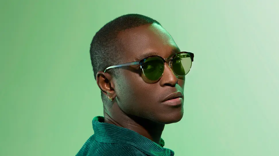 Black man wearing green tinted sunglasses on green background