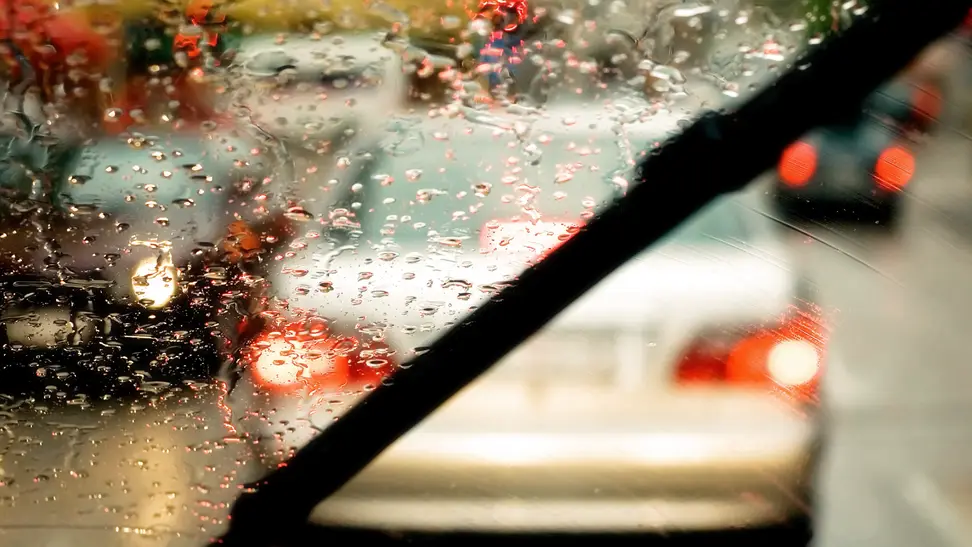 Close-up of a windshield wiper blade clearing away the rain from one side, a painterly cityscape visible beyond the windshield.