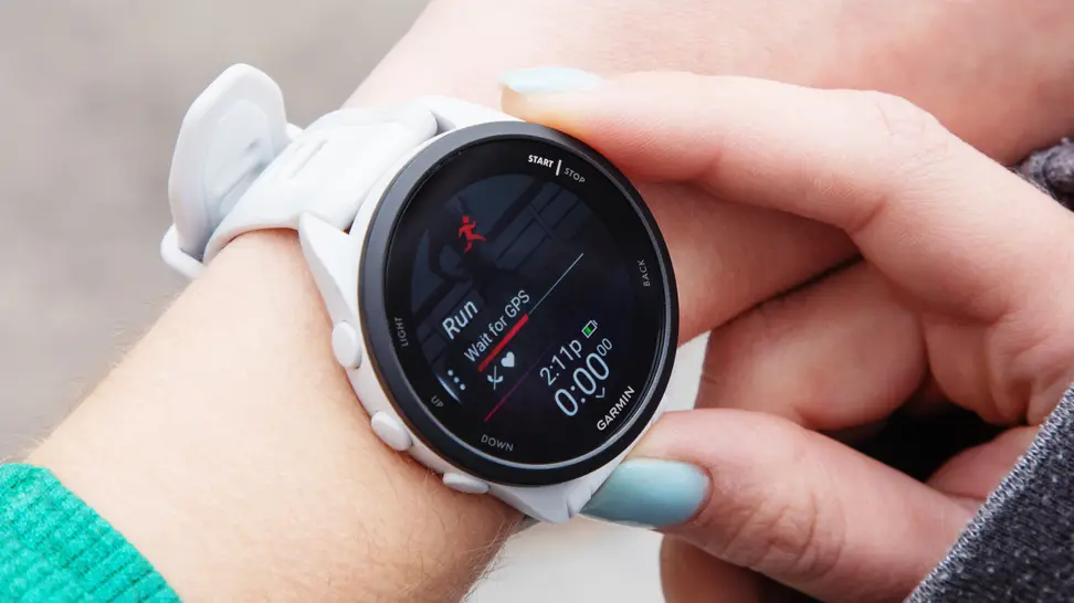 A woman holding a white, Garmin Forerunner 165 watch attached to her wrist.