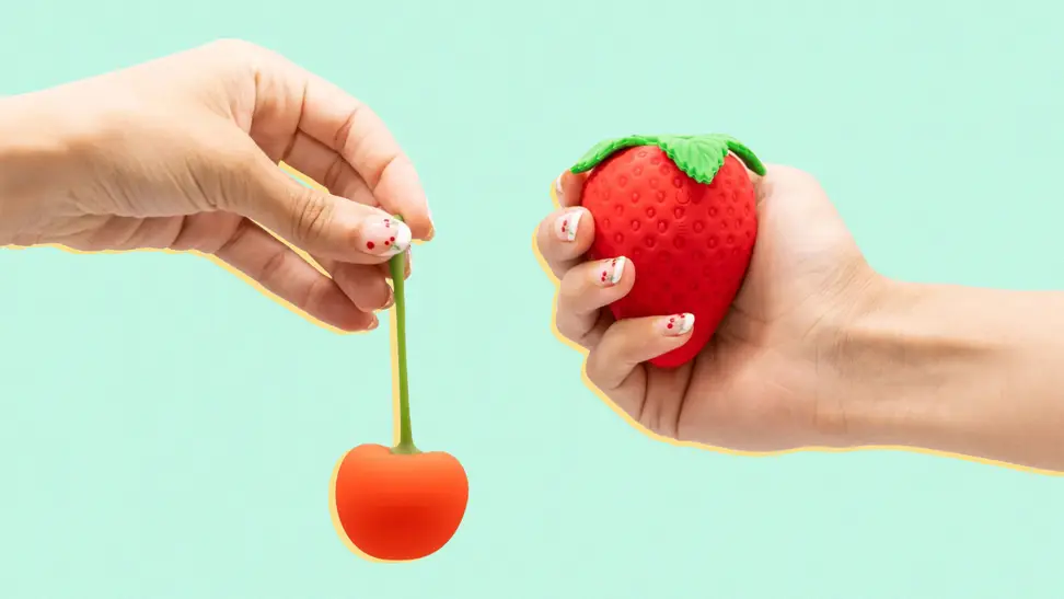 A hand holding the cherry Emojibator next to a hand holding the strawberry Emojibator