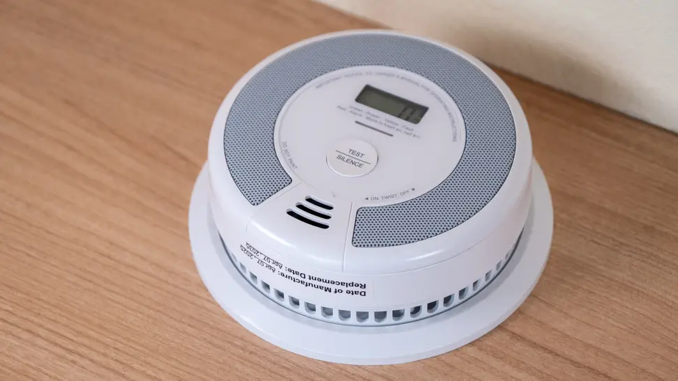 A round, white smoke detector sits on a wood background