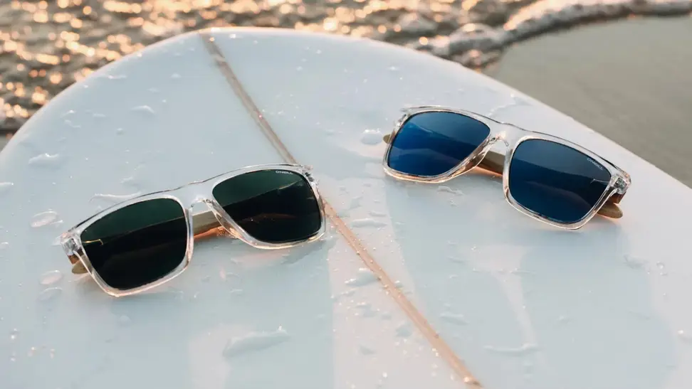 2 pairs of O'Neill x GlassesUSA.com Harwood 2.0 glasses sit on a surfboard in the sand
