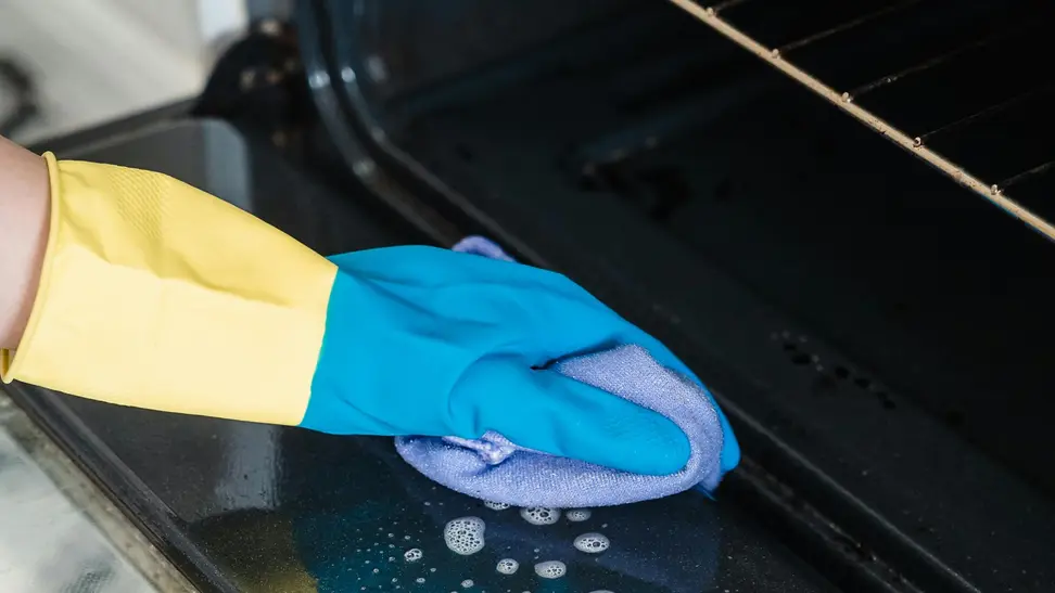 Person wearing a glove cleans an oven