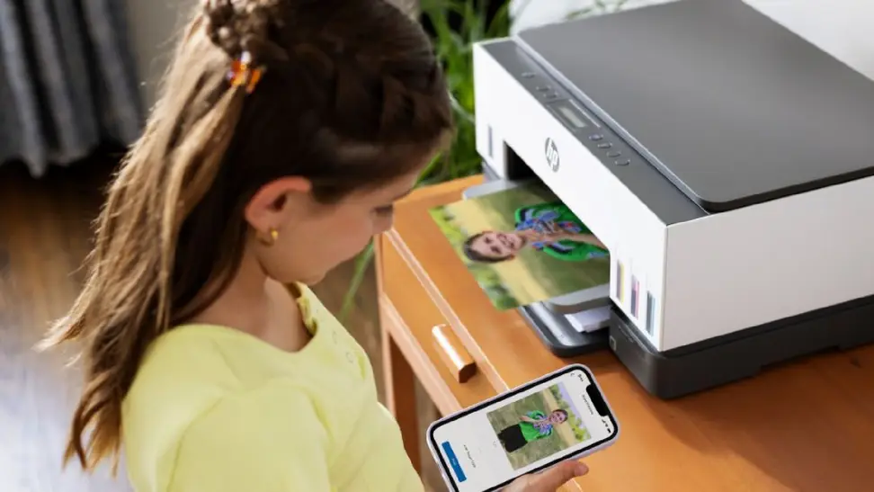 Younf girl looks at her phone as the HP catridge-free printer prints it out in color